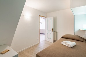 Une chambre à coucher comprenant un lit, une table de chevet, un miroir et une porte donnant sur une autre pièce.