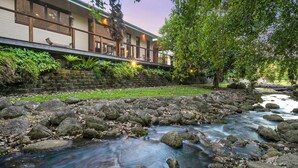 A riverside view with a stone wall, a wooden deck, and a building with large windows. - Figtree Villas Palm Cove (Palm Cove)
