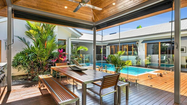 A modern outdoor deck with a pool, wooden furniture, and tropical plants. - Figtree Villas Palm Cove (Palm Cove)