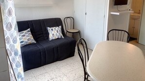 Ein gemütlicher Wohnraum mit einer Couch, zwei Sesseln, einem kleinen Tisch, einem Fernseher und einem sichtbaren Badezimmer im Hintergrund.
