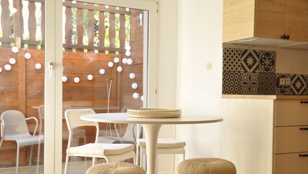 Una cocina moderna con armarios blancos, un salpicadero con diseño y una zona de comedor con una mesa redonda y dos taburetes.