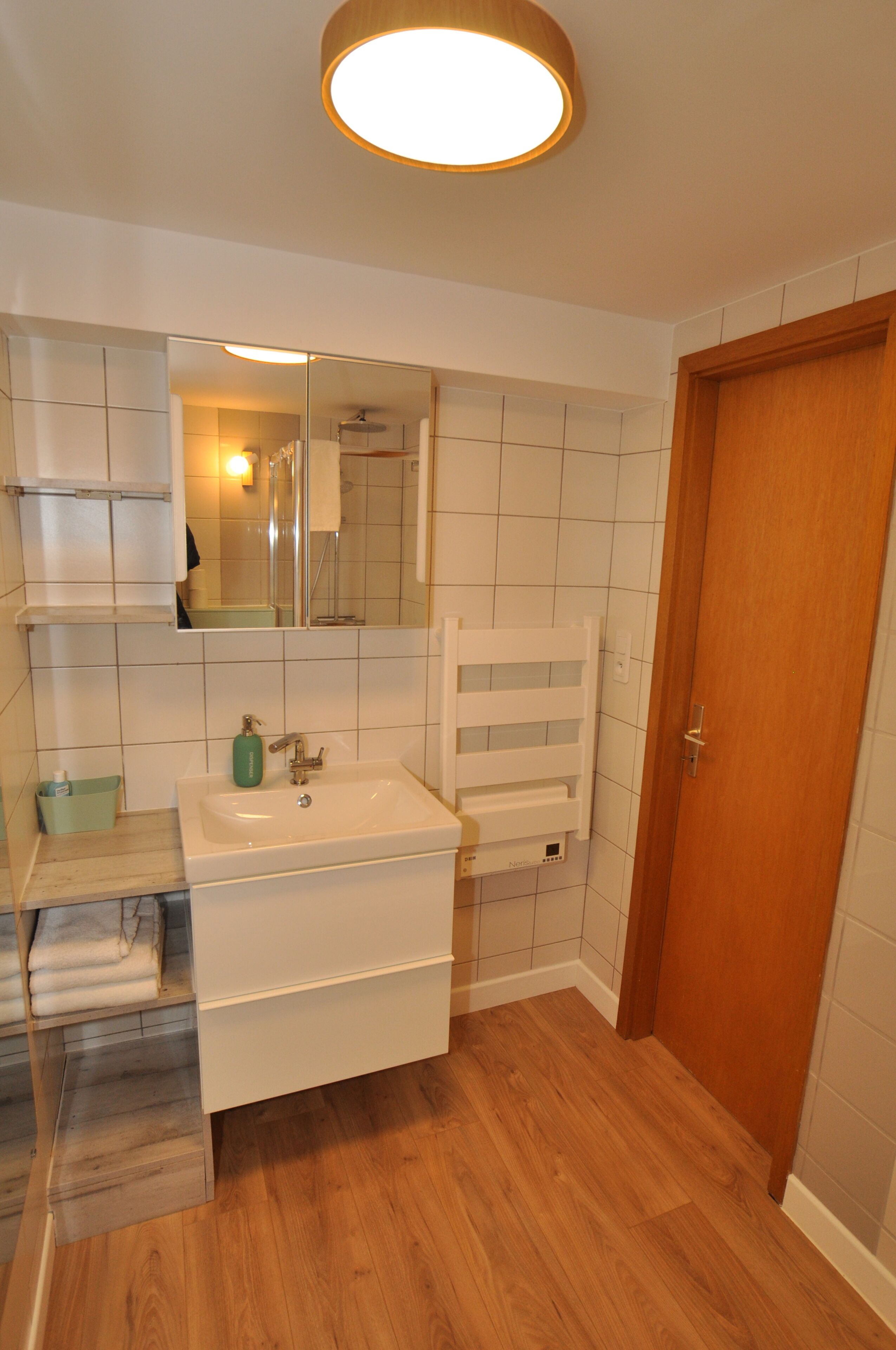 Un bagno con lavandino bianco, specchio e porta in legno.