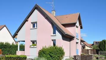 Une maison à deux étages, avec un toit en pente et une cheminée. Un panneau indique les instructions de stationnement.