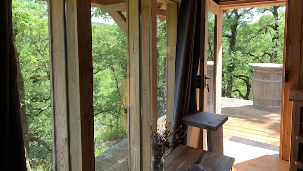 A wooden cabin with large windows, a wooden deck, and a view of a forest. - L'Hermitage, an old stone shepherd's hut (Salvagnac-Cajarc)