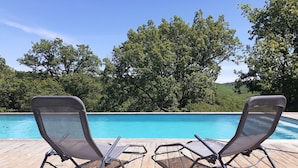 Two lounge chairs facing a swimming pool with a wooden deck and a backdrop of trees. - L'Hermitage, an old stone shepherd's hut (Salvagnac-Cajarc)