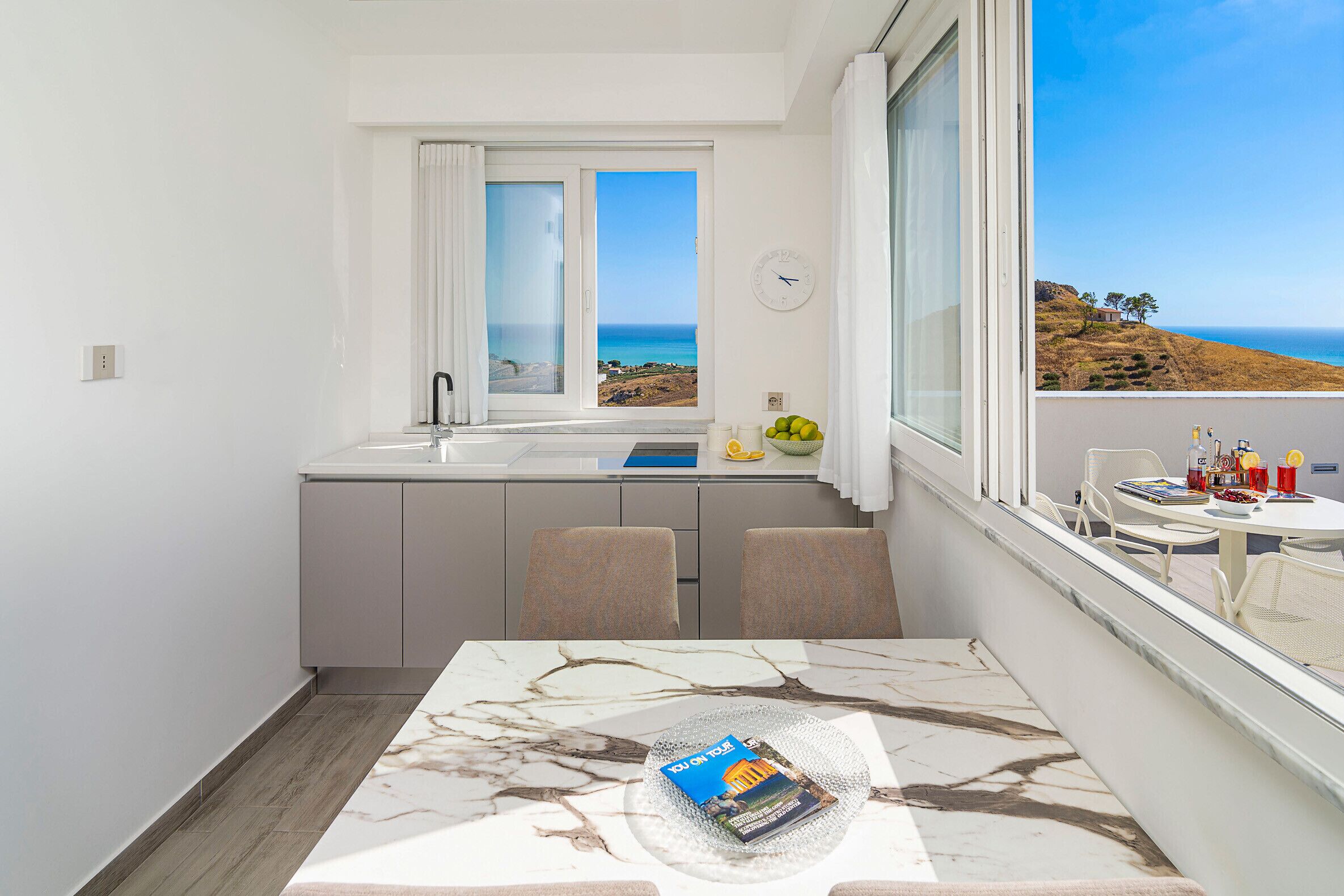 Una cucina compatta con vista sul mare, un'area pranzo con tavolo e una finestra con tende.
