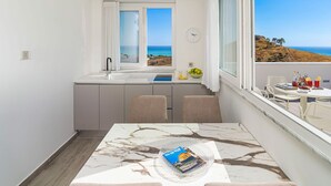 Et kompakt køkken med havudsigt, et spiseområde med et bord og et vindue med gardiner.