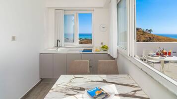 Una cucina compatta con vista sul mare, un'area pranzo con tavolo e una finestra con tende.