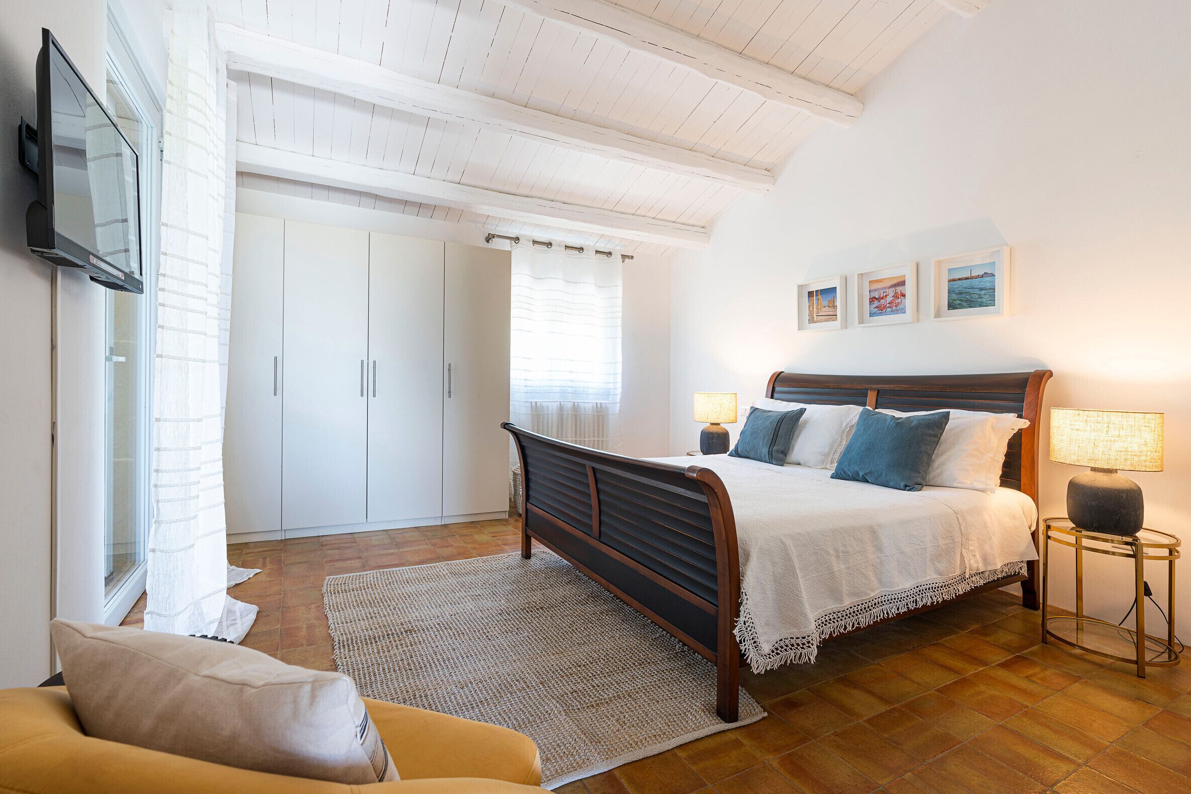 Une chambre à coucher avec un lit, des lampes de chevet, une télévision et une fenêtre avec des rideaux.