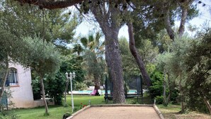 Un court de tennis en terre battue, entouré d’arbres, avec un bâtiment visible au fond.