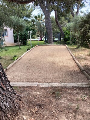 A gravel court with surrounding trees and a building in the background.
