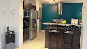 Une cuisine moderne dotée d’appareils électroménagers en acier inoxydable, d’un mur d’accent de couleur turquoise et d’un coin bar avec des tabourets.