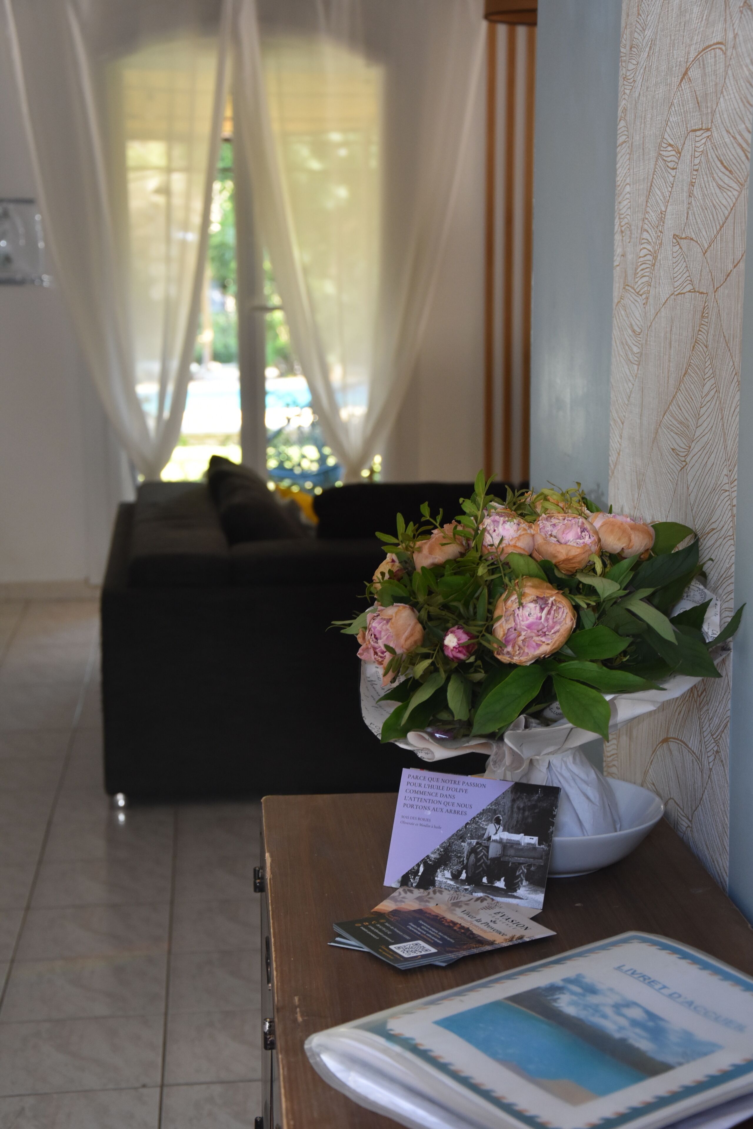 A room with a sofa, a table with a vase of flowers, and a wall with a patterned wallpaper.