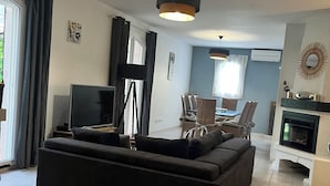 Un salon moderne avec un canapé noir, un téléviseur à écran plat et un coin repas doté de chaises en osier.