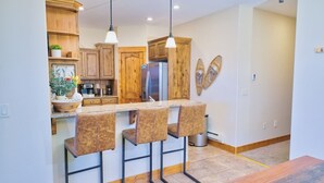 Una cocina moderna con gabinetes de madera, un refrigerador de acero inoxidable y una zona de bar con taburetes.