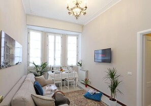 A living room with a sofa, a dining table, and a TV mounted on the wall. - Liberty Rome Apartment (Roma)