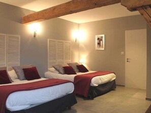 Une chambre à coucher avec deux lits, chacun recouvert d’une couverture rouge et agrémenté d’oreillers, une poutre en bois au plafond et un luminaire fixé au mur.