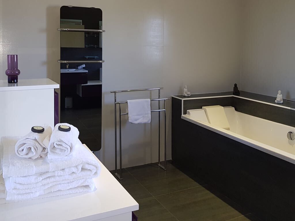 Ein modernes Badezimmer mit einer großen Badewanne, einem Waschtisch inklusive Spiegel und einem Handtuchhalter.