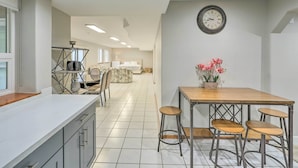 A modern kitchen with a white countertop, a wooden dining table with bar stools, and a clock on the wall. - Spacious Kent Home: Great for Large Families! (Kent)