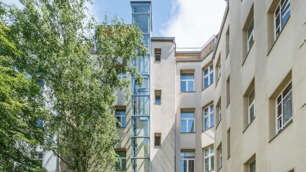 A multi-story residential building with a central staircase, surrounded by greenery and other buildings. - Boxi Top-floor Apartment (Berlin)