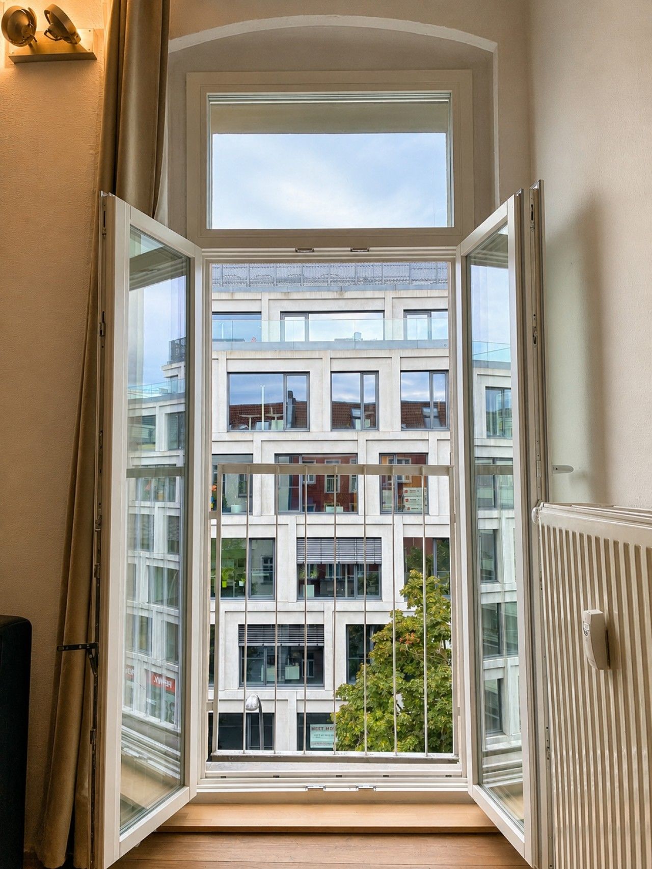 Ein Zimmer mit großem Fenster, Heizkörper und Blick auf ein mehrstöckiges Gebäude.