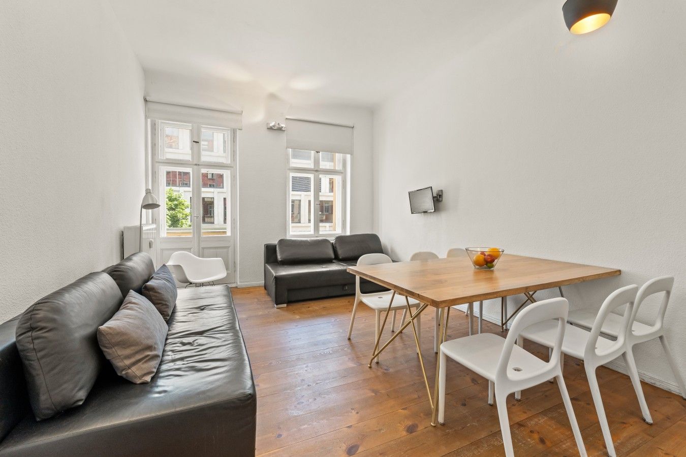 Ein modernes Wohnzimmer mit einer Couch, einem Esstisch mit Stühlen und einem an der Wand montierten Fernseher.