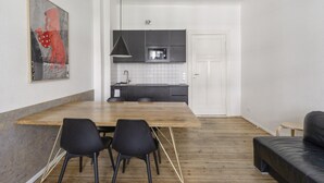 Une cuisine moderne avec des meubles de couleur sombre, un four à micro-ondes et un évier. On y trouve également un coin repas avec une table en bois et des chaises noires.
