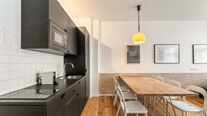 A modern kitchen with black cabinets, a wooden dining table, and a yellow pendant light. - Boxi 6 pax - Roomy Apartment with balcony (Berlin)