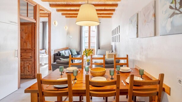 Un comedor con una mesa y sillas de madera, una lámpara colgante y un sofá al fondo.