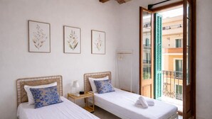 Una habitación con dos camas, una mesita de noche con lámpara, y un cuadro con motivos florales en la pared.