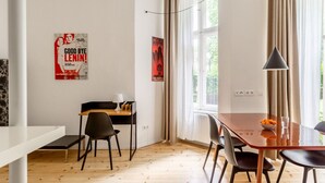A modern room with a wooden floor, a dining table with chairs, a small desk with a lamp, and two posters on the wall. - Boxi Beautifull Studio with patio (Berlin)