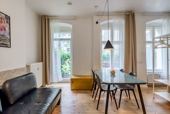 A modern living room with a glass dining table, black leather sofa, and a yellow bench.