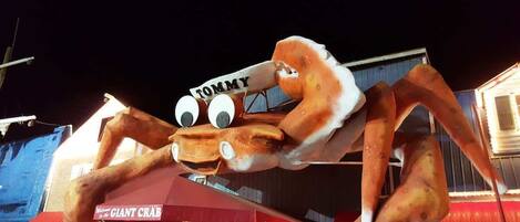 A large crab mascot with a sign that reads "TOMMY" in front of a building with a red awning and a sign that says "GIANT CRAB".