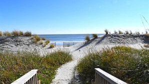 Ein Sandweg am Strand, der zum Meer führt, mit einem Holzzaun an einer Seite.