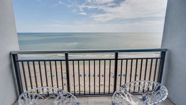 Ein Balkon mit Blick auf den Strand, Metallstühle und einem Geländer.