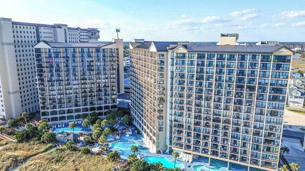 A high-rise hotel with multiple balconies, a swimming pool, and a view of the surrounding area. - Newest at Beach Cove,Updated Ocean Front,Low Floor (North Myrtle Beach)