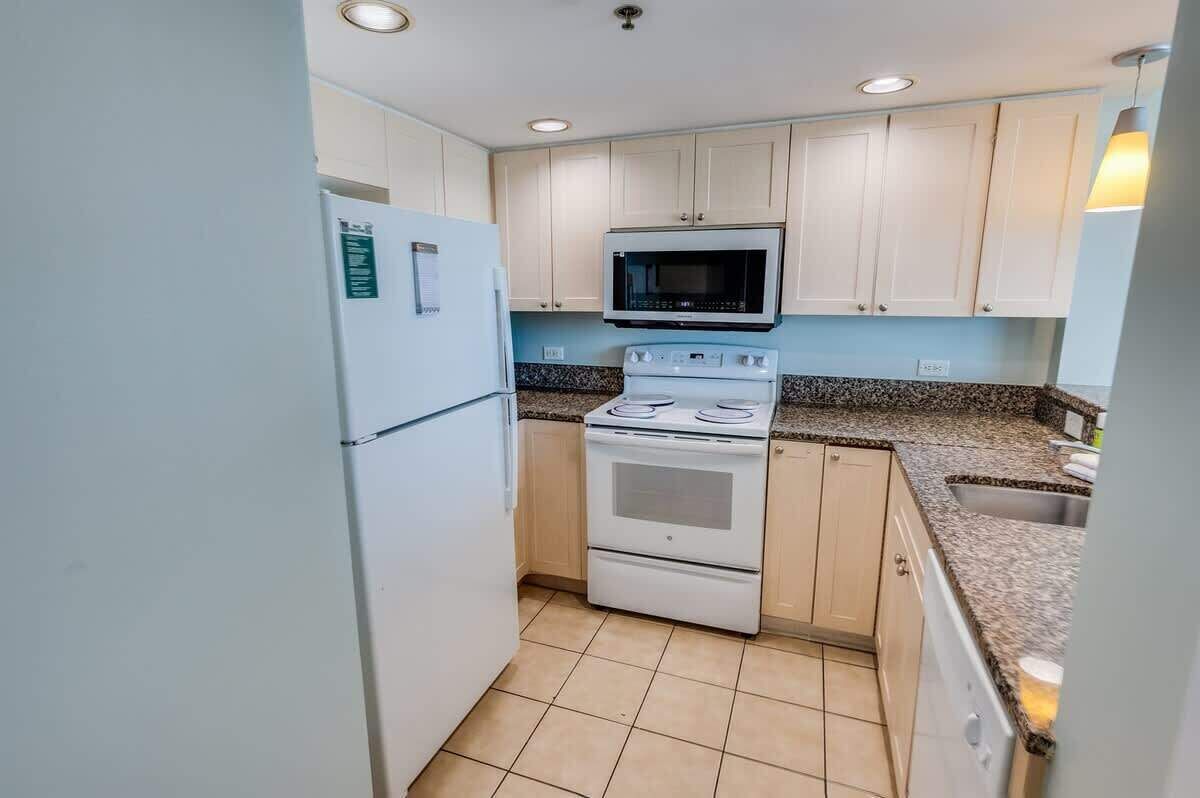 A compact kitchen with white cabinets, a microwave, a stove, and a refrigerator.