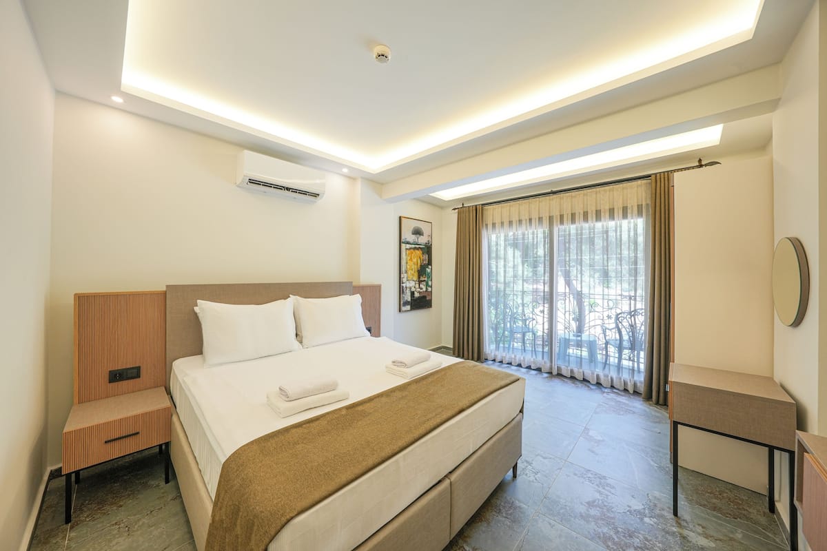 A modern hotel room with a large bed, a bedside table, a desk, and a window with curtains.