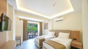 A modern hotel room with two beds, a TV, a desk, and a balcony with a view of greenery. - Ada Butik Hotel (Marmaris)