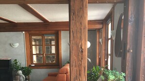 A cozy living room with a white sofa, an orange armchair, and a wooden table with potted plants. A large wooden beam is prominently featured in the foreground. - Comfortable apartment in alsatian house (Oberbronn)