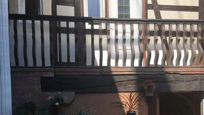 A traditional half-timbered building with a balcony, potted plants, and a cobblestone ground. - Comfortable apartment in alsatian house (Oberbronn)