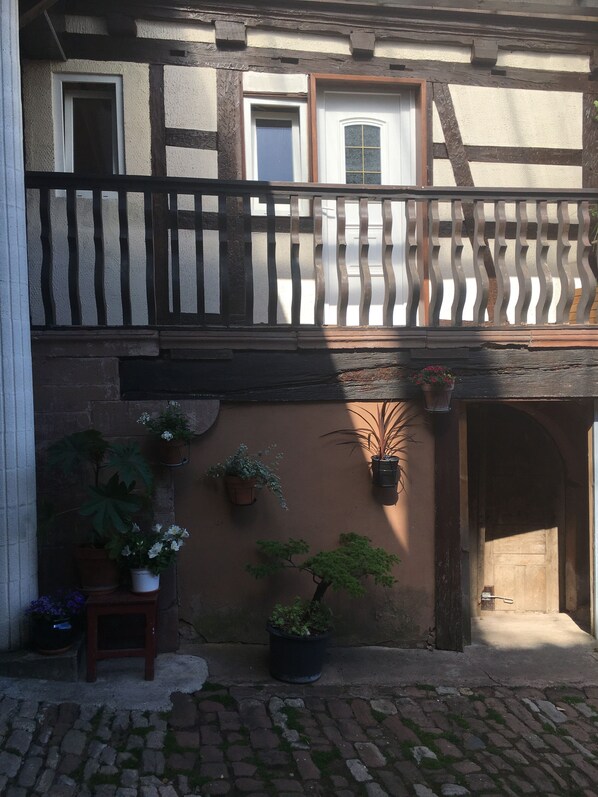 Ein traditionelles Fachwerkhäuschen mit Balkon, Blumentöpfen und Kopfsteinpflaster.