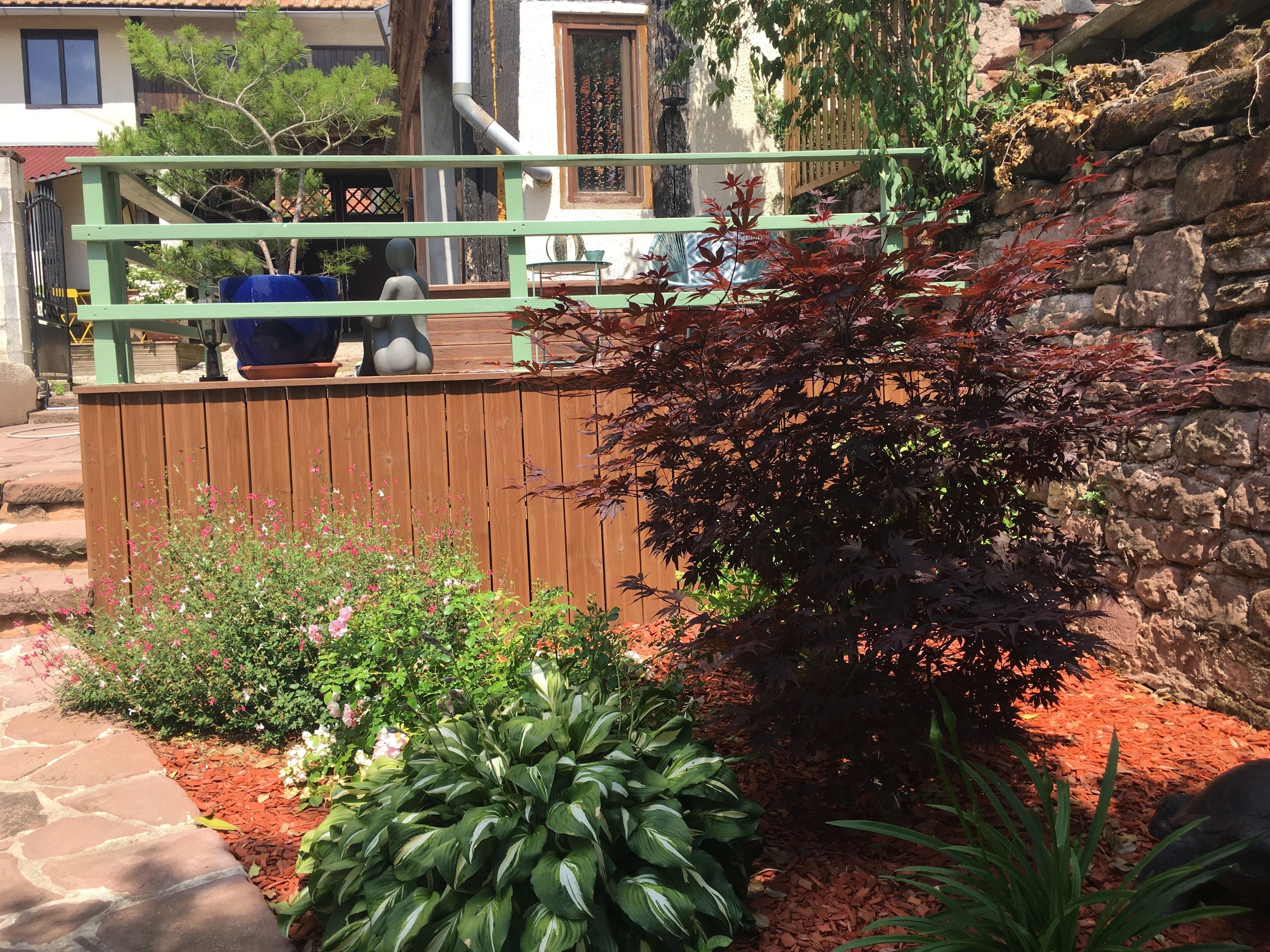 A garden with a wooden fence, a stone wall, and various plants.