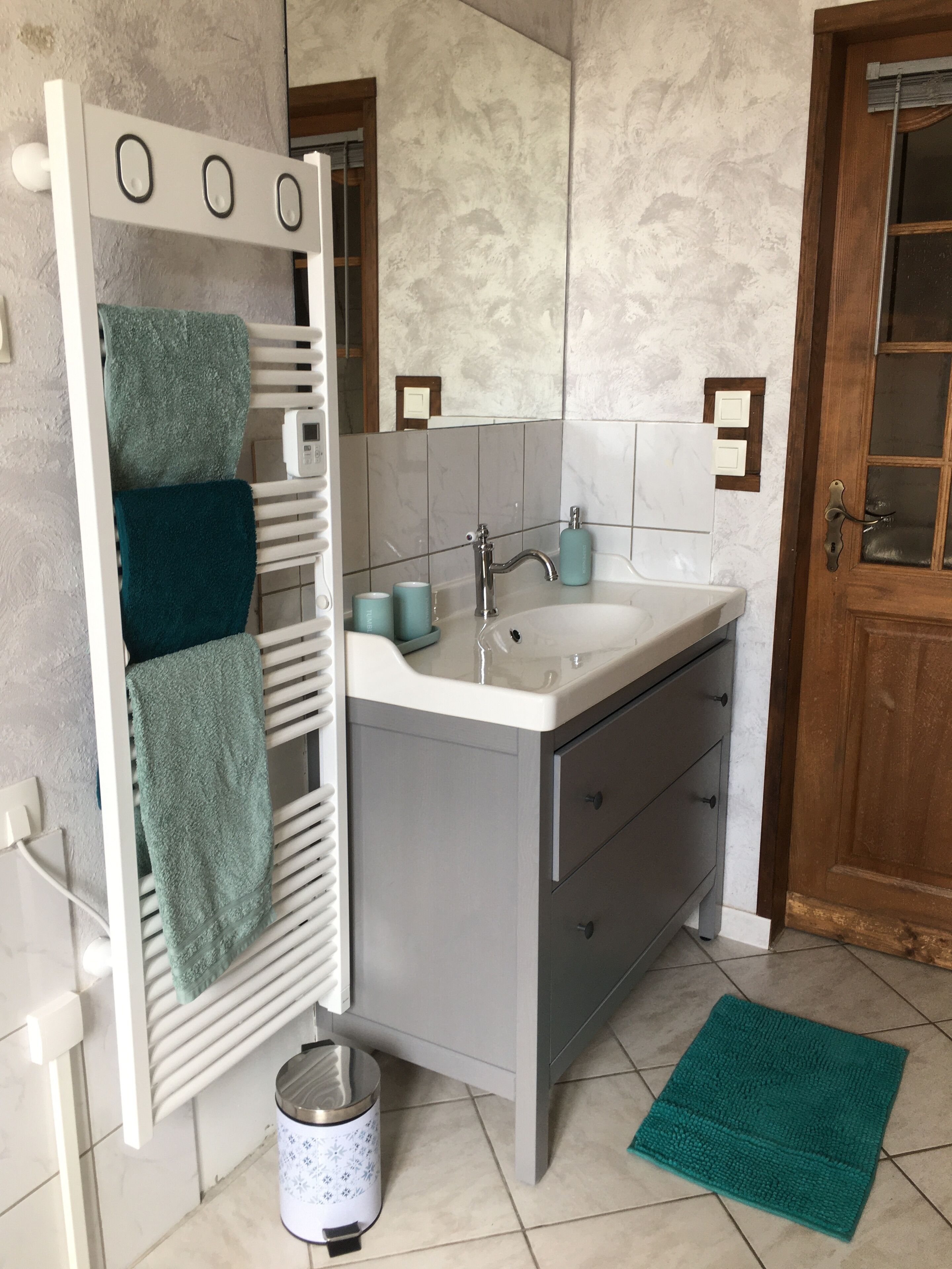 A bathroom with a white sink, grey cabinet, and a wooden door.