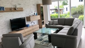 Un salon moderne avec un canapé d’angle, une table basse en verre et un téléviseur à écran plat posé sur une console en bois.