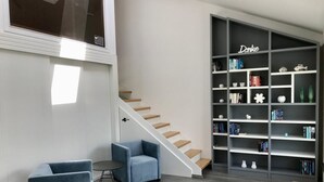 Un salon moderne avec un escalier, une bibliothèque et deux fauteuils bleus.