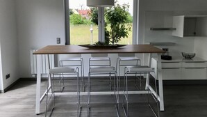 Une cuisine moderne avec un îlot central en bois, des tabourets de bar blancs et une vue sur un jardin grâce à une grande fenêtre.