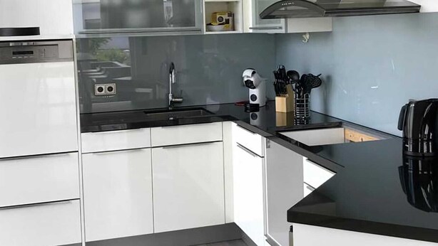 Une cuisine moderne avec des meubles blancs, un plan de travail noir et une hotte en acier inoxydable.