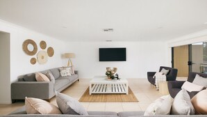 Una sala de estar moderna con un sofá gris, una mesa de centro blanca y un televisor montado en la pared.