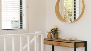 Una habitación con barandal blanco, una mesita de madera con espejo y una ventana con persianas.